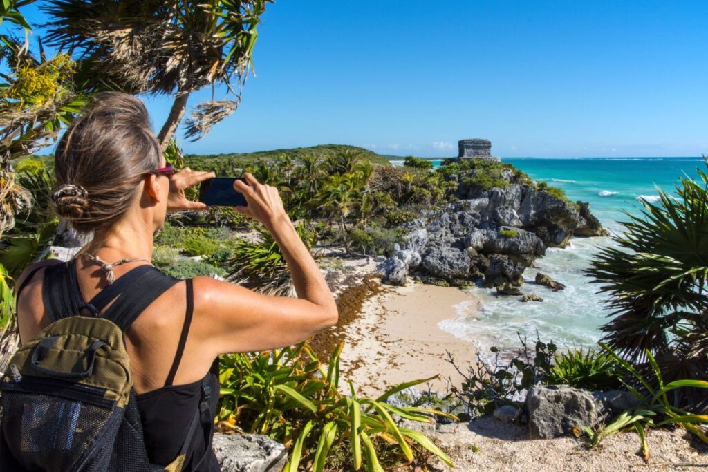 A woman taking a photo of the Mayan Ruins in Tulum Mexico